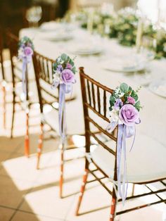 purple flowers are tied to the back of chairs at an outdoor wedding dinner table with place settings