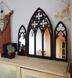 three arched mirrors on top of a wooden dresser next to a potted plant and mirror