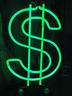 a neon green dollar sign sitting on top of a black table in a dark room