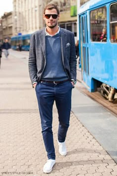 a man walking down the street in front of a blue train with his hands in his pockets