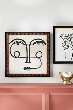 two framed pictures hang on the wall next to a pink dresser and vase with flowers