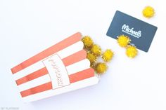 two popcorn boxes with yellow pom - poms next to a black and white business card