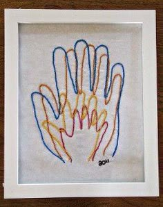 an embroidered handprint in a white frame on a wooden table with a brown background