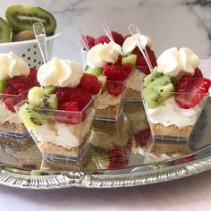 four desserts are arranged on a silver platter with strawberries and kiwi