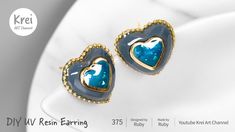 two heart shaped earrings with blue and gold accents on a white plate, one is in the shape of a heart