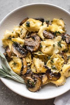 a white bowl filled with pasta and mushrooms on top of a table next to a fork