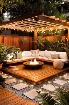 an outdoor living area with wooden decking and lights strung over the fire pit, surrounded by greenery