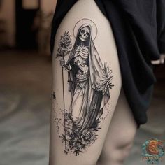 a woman's thigh with a skeleton and flowers tattoo on her leg, holding a cross