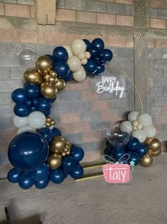 blue and gold balloons are arranged in the shape of a wreath on a brick wall