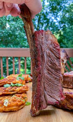 a person holding up a piece of meat on a cutting board next to other food