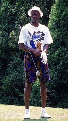 a man standing on top of a lush green field holding a golf ball and club