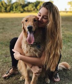 a woman is hugging her dog on the grass with its tongue out and it looks like she has long hair