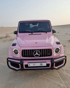 a pink mercedes g - class is parked in the middle of sand dunes with its hood up