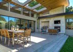 an outdoor dining area with wooden chairs and table in front of a large glass window