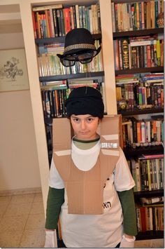 a young boy wearing a cardboard box costume in front of a bookshelf full of books