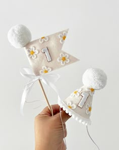 a hand holding two small white hats with pom poms on top of them