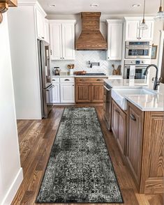 a kitchen with wooden floors and white cabinets, an area rug in the middle of the floor