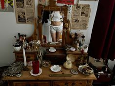 a dresser with a mirror and various items on it in front of a woman's reflection