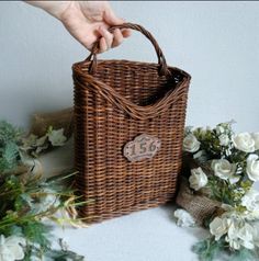 a person holding a brown wicker basket next to white flowers