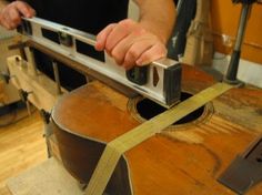 a man is working on a guitar in his shop with a measuring tape around the neck