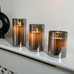 three candles sitting on top of a white shelf