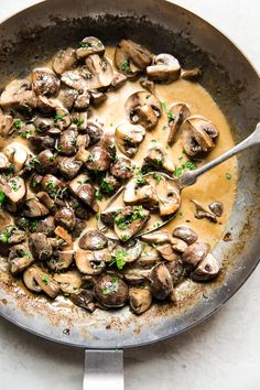 a skillet filled with mushrooms and gravy on top of a white table