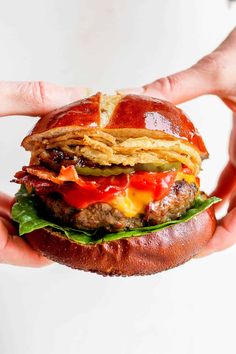 a hand holding a hamburger with bacon, lettuce and tomato on it in front of a white background