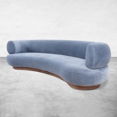 the curved sofa is made from blue velvet and has a wooden foot rest on it