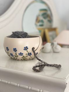 a white bowl with blue flowers on it sitting on a dresser next to a mirror