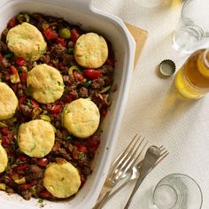 a casserole dish filled with meat, vegetables and dumplings next to silverware