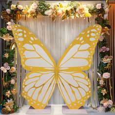 a large yellow butterfly sitting on top of a white floor next to flowers and greenery