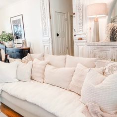 a living room filled with lots of white furniture and pillows on top of a couch