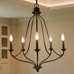 a chandelier with five lit candles hanging from it's center piece in a dining room