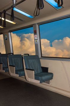 the inside of a train car with blue seats and windows looking out at white clouds