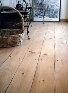 a wooden floor in a room with pictures on the wall and a wicker basket next to it