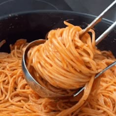 spaghetti being cooked in a pot with two tongs sticking out of the top one