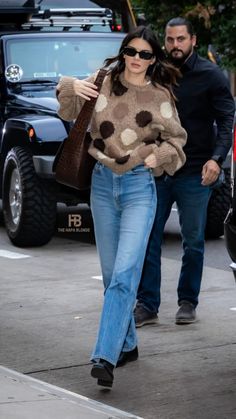 a woman walking down the street wearing jeans and a sweater with polka dots on it