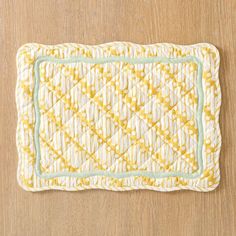 a yellow and white placemat on a wooden surface with a green border around the edge