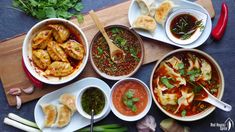 several bowls of food are arranged on a cutting board with chopsticks and spoons