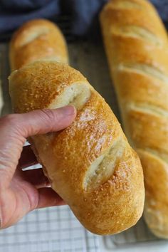 a person holding a piece of bread in front of two loaves on a cooling rack