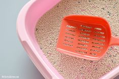 an orange plastic scooper sitting on top of a pink litter box filled with sand