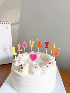 a birthday cake with candles that spell out i love you on it and a calendar in the background