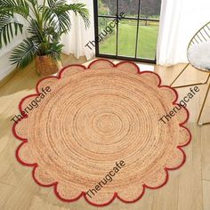 a round rug with red trim on the floor in front of a window and potted plant