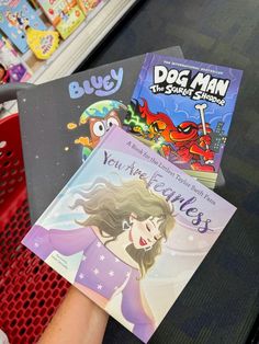 two children's books sitting on top of a red shopping cart in a store