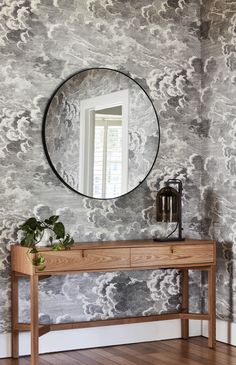 a wooden table with a mirror on it in front of a wallpapered wall