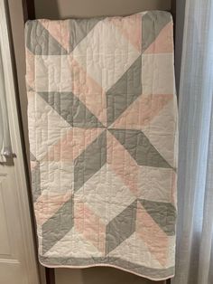 a pink and grey quilt hanging on a wall