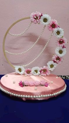 a pink cake with pearls and flowers on it sitting on a blue tablecloth next to a wall