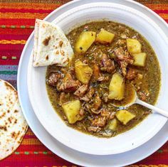 a white bowl filled with soup next to two pita bread on a colorful table cloth