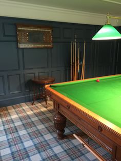 a green pool table in the corner of a room with two stools and a lamp