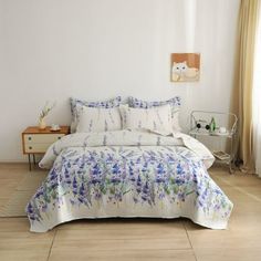 a white bed with blue flowers on it in a room next to a wooden floor